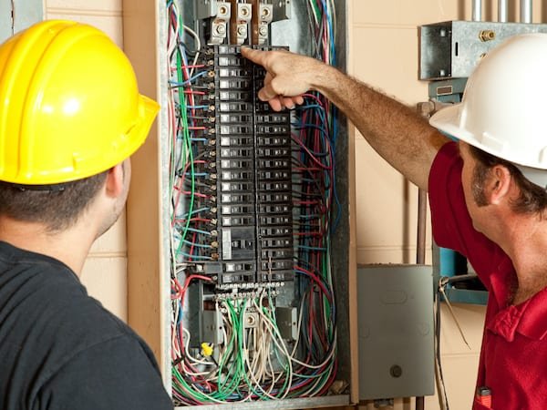Licensed electricians inspecting a residential electrical breaker panel inside a home